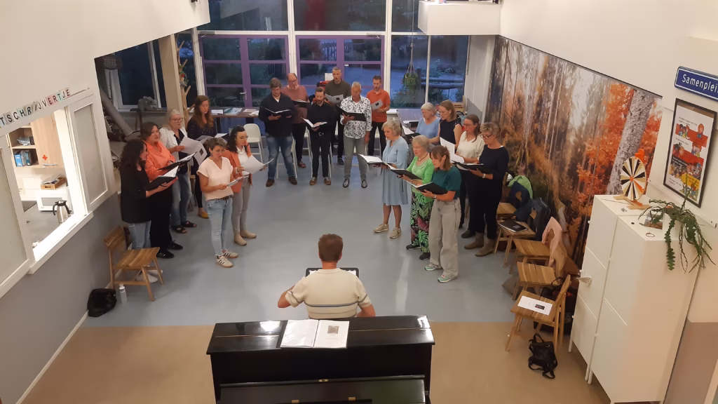 Een repetitie met het Gelders Vocaal Ensemble. Het koor staat in een halve cirkel, de dirigent begeleidt waar nodig op piano.